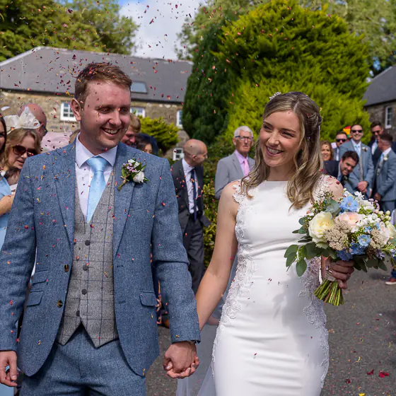 Bride and groom smiling and walking through falling confetti at a Pembrokeshire wedding venue, captured by Dick Lloyd Photography