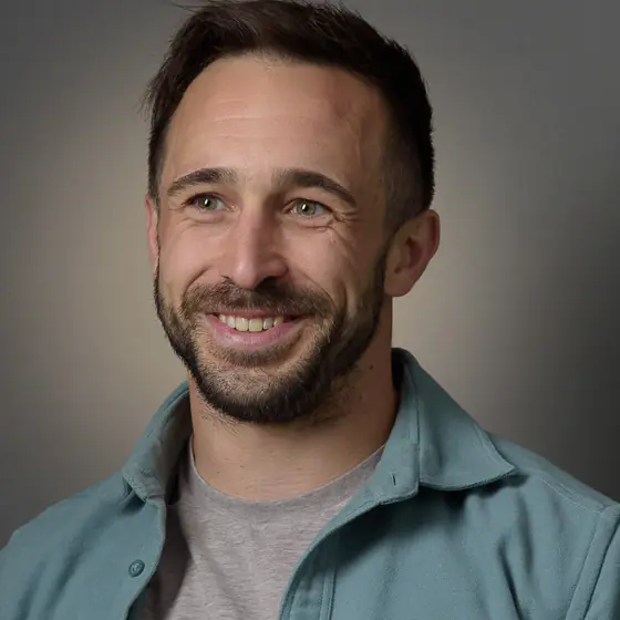 Confident, approachable man smiling in a professional studio headshot with a grey background