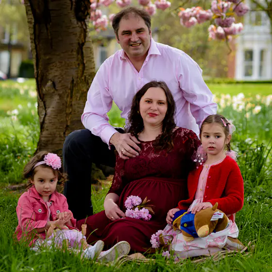 Family including two young daughters sitting beneath a cherry tree in blossom