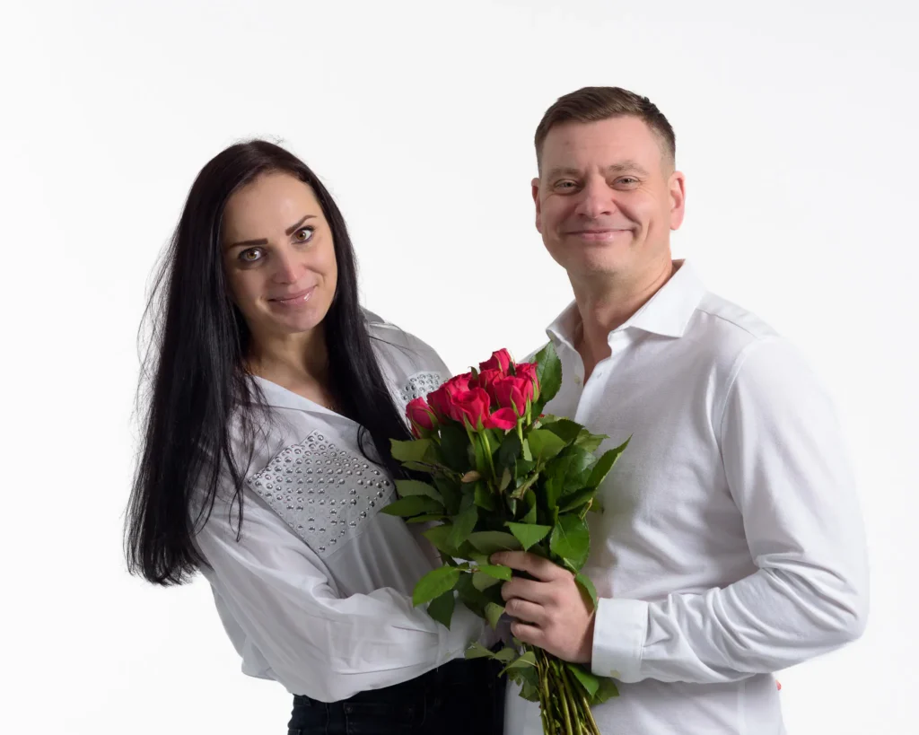 A studio image of a couple with a bunch of red roses, white background. captured by Dick Lloyd Photography 