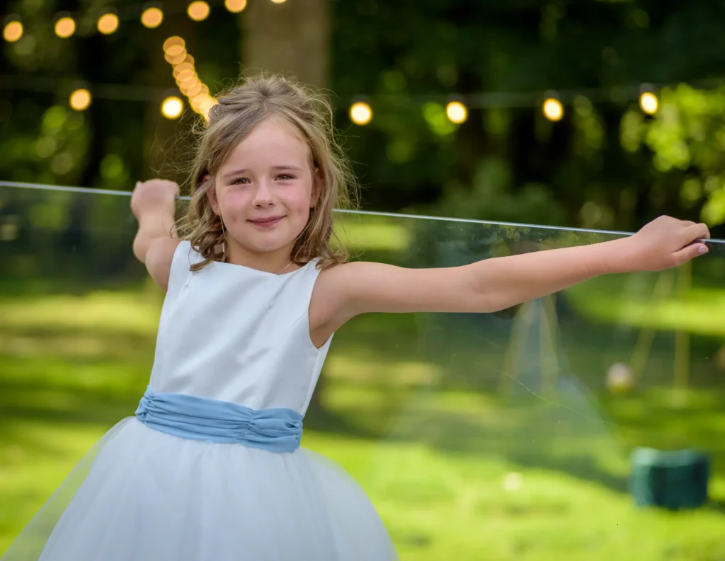 Angharad & Lewis Wedding-1107 Smiling flower girl in white dress with blue sash and fairy lights in background, Pembrokeshire wedding photography by Dick Lloyd Photography