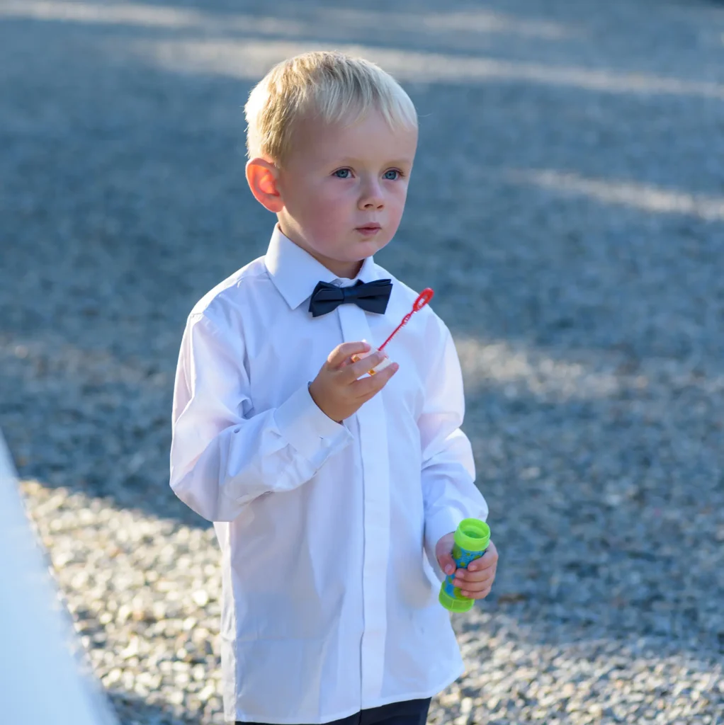 Angharad & Lewis Wedding-1448 Young boy in white shirt blowing bubbles at outdoor reception, Pembrokeshire wedding photography by Dick Lloyd Photography
