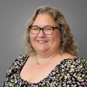 Woman wearing floral dress and glasses - headshot with grey background